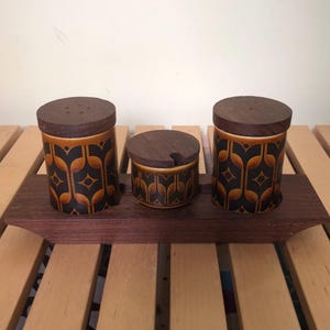 May include: A vintage ceramic salt and pepper set and a sugar bowl with a wooden spoon, displayed on a wooden tray. The set features a brown, black, and tan geometric pattern. The lids are made of dark wood.