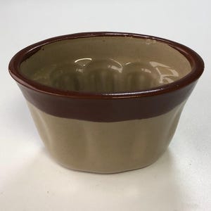 May include: A two-tone ceramic pudding basin. The rim and top section are dark brown, with a lighter tan colour on the lower part. The interior features a fluted design.