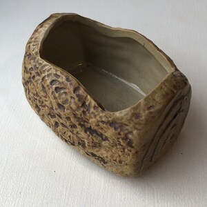 May include: A brown ceramic planter shaped like a log with a rough, textured surface.