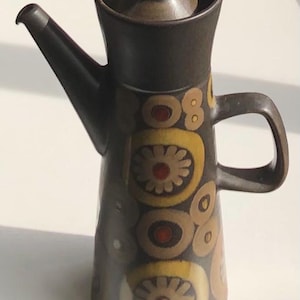 May include: A dark brown ceramic coffee pot with a lid and a handle. The pot is decorated with yellow, brown, and red floral patterns. The spout is on the left side.
