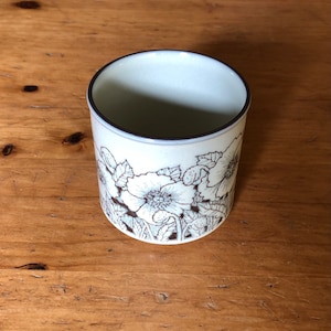 May include: A white ceramic mug with a brown floral design. The mug has a brown rim and a white interior.