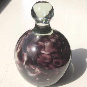 May include: A purple glass bottle stopper with a clear glass top. The bottle stopper has a swirling pattern of white and purple.