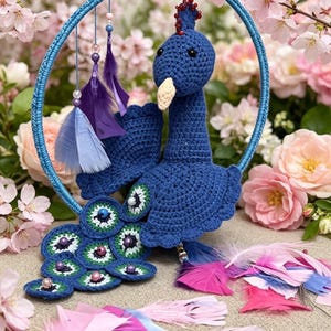 May include: A blue crocheted peacock ornament suspended within a matching blue circular frame. The peacock features a detailed tail with green and white circular accents, small beads, and hanging purple and light blue feathers attached to the frame.