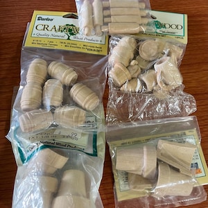 May include: Assortment of small, unfinished wooden craft pieces in clear plastic bags. Includes miniature barrels, rolling pins, and other shapes. Packages are labeled "Craftwood" and "Quality Natural Wood Products".