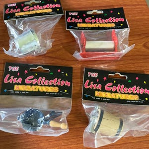 May include: Four miniature toys from "The Lisa Collection" are packaged in clear plastic. The toys include a metal bucket, a red and white roller, a blue and white pan with a wooden handle, and a wooden barrel.