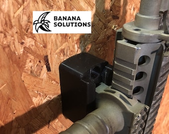 May include: A black gun wall mount with a rifle attached. The rifle is a dark green color with a black handgrip. The wall mount is attached to a wood panel.