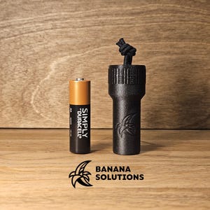 Puede incluir: Un tapón de botella de plástico negro con un cordón negro y un logotipo de plátano. El tapón de botella está al lado de una pila AA marrón con el texto "SIMPLY DURACELL" en el lateral.