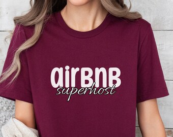 May include: Maroon crew neck t-shirt with the text "airBNB superhost" in white. The shirt is a solid maroon color and has short sleeves. The text is in a sans-serif font.