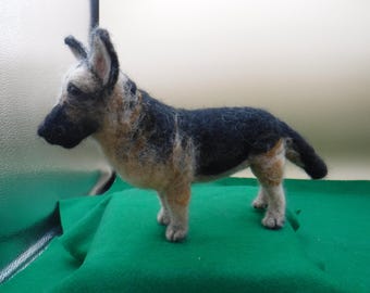 May include: A hand-felted German Shepherd dog figurine. The dog is standing on a green surface and is made of wool. The dog is brown, black, and white.