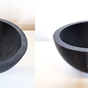 May include: A dark gray, semi-spherical bowl with a textured interior and a smooth, rounded rim. The bowl is made of a solid material and sits on a white surface. The design is simple and modern, suitable for various uses.