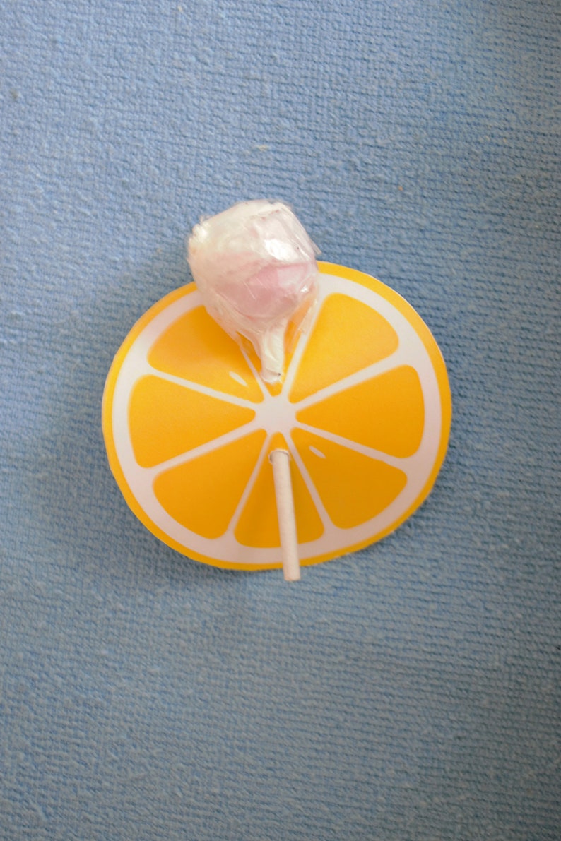 Op de afbeelding: Een gele citroenschijf-lolly met een roze en witte lolly erop.