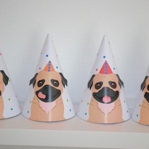 Puede incluir: Cuatro gorros de fiesta blancos con un diseño de cara de carlino. Cada gorro tiene un gorro de fiesta de color y estampado diferente en la parte superior. Los carlinos sonríen todos con la lengua fuera.