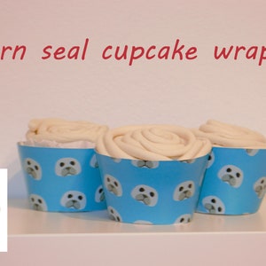 May include: Three white frosted cupcakes with blue cupcake wrappers featuring a pattern of white seal faces. The wrappers have the text "Spiral Printables" on a white circle.