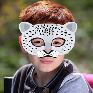 Puede incluir: Un niño con una máscara de leopardo de las nieves gris y negro. La máscara tiene manchas negras y una nariz y bigotes blancos.
