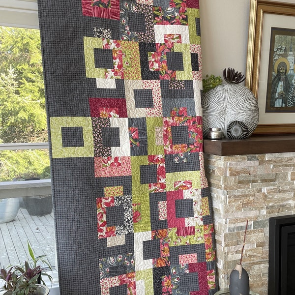 Modern large quilt in floral pinks, cranberry, chartreuse, gray designer fabric blocks that float on a dark gray thatched background.