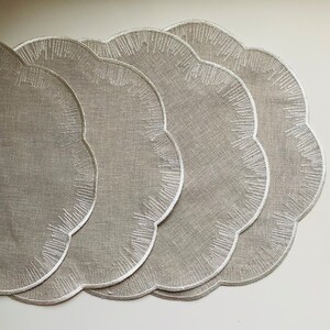 Puede incluir: Juego de cuatro manteles individuales de lino beige con bordes festoneados y dise&ntilde;os bordados en blanco.