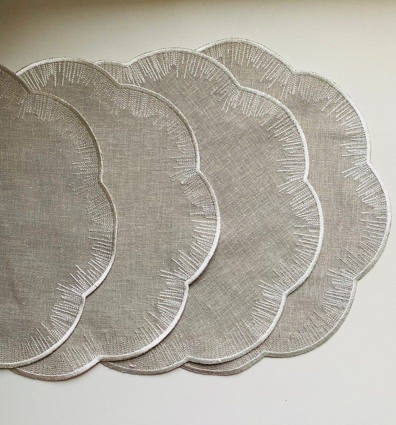 Puede incluir: Juego de cuatro manteles individuales de lino beige con bordes festoneados y dise&ntilde;os bordados en blanco.