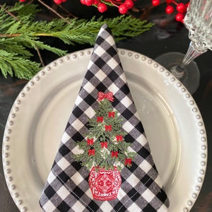 Può includere: Tovagliolo di stoffa a quadri bianchi e neri con un albero di Natale ricamato in un vaso rosso con un fiocco rosso. L'albero è decorato con palline rosse.