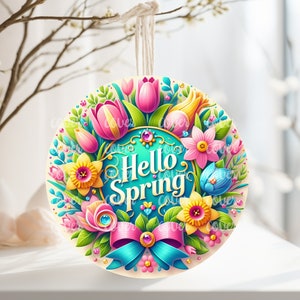 May include: A round, colorful spring-themed ornament with a blue background and the text "Hello Spring" in a gold font. The ornament is decorated with pink, yellow, and blue flowers, green leaves, and a blue bow with a pink ribbon.