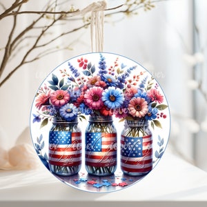 May include: Three glass mason jars with red, white, and blue American flag designs are filled with a bouquet of pink, blue, and purple flowers. The jars are sitting on a white surface with blue and red stars scattered around them.