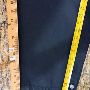 K&ouml;nnte beinhalten: Schwarze Hose mit Knopfdetail. Das Kleidungsst&uuml;ck wird mit einem Lineal gemessen und zeigt eine L&auml;nge von etwa 86 cm. Der Stoff scheint eine einfarbige, dunkle Farbe zu haben.