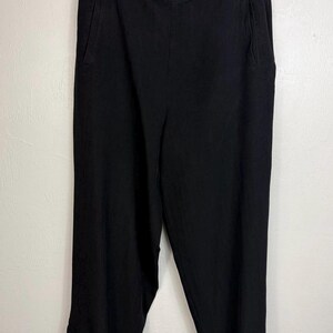K&ouml;nnte beinhalten: Schwarze, knielange Hose mit hoher Taille und Seitentaschen. Die Hose hat ein Knopfdetail am Saum und h&auml;ngt an einem schwarzen Kleiderb&uuml;gel. Der Stoff scheint ein leichtes Material zu sein.