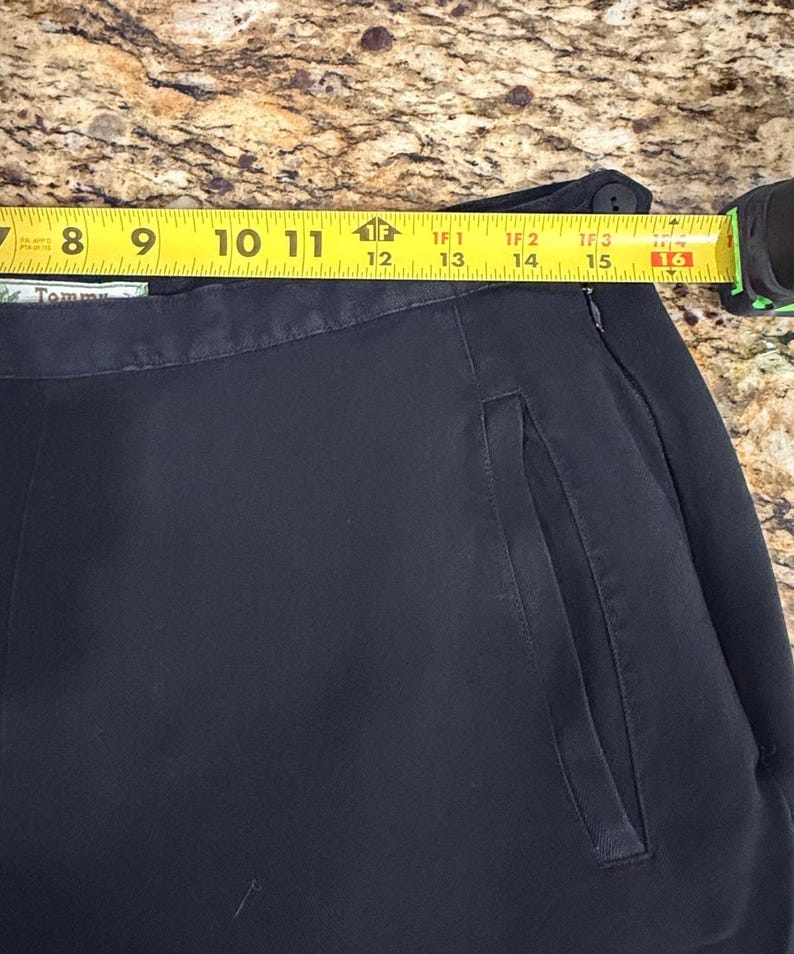 K&ouml;nnte beinhalten: Nahaufnahme einer marineblauen Hose mit einer Seitentasche. Ein gelbes Ma&szlig;band zeigt eine L&auml;nge von etwa 38 cm an. Die Hose ist dunkelblau.
