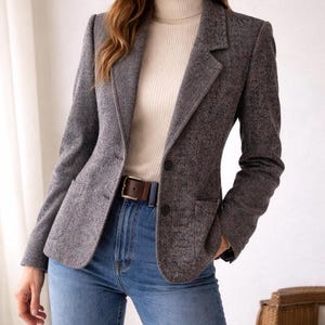 May include: A gray tweed blazer with a notched lapel, two-button closure, and front pockets. The blazer is paired with a cream-colored turtleneck sweater, blue jeans, and a brown leather belt. The outfit is completed with a brown leather belt.