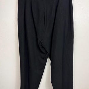 K&ouml;nnte beinhalten: Schwarze Hose an einem schwarzen Kleiderb&uuml;gel. Die Hose besteht aus einem einfarbigen schwarzen Stoff. Sie hat eine hohe Taille und ein weites Bein. Ein klassischer Stil.