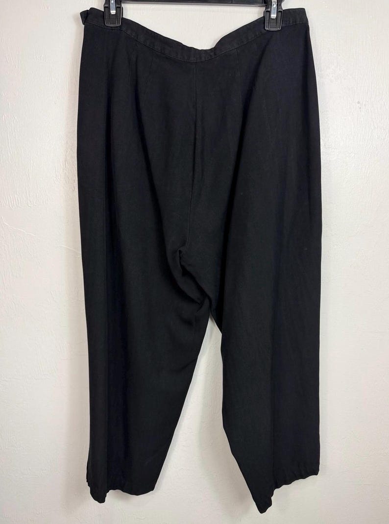 K&ouml;nnte beinhalten: Schwarze Hose an einem schwarzen Kleiderb&uuml;gel. Die Hose besteht aus einem einfarbigen schwarzen Stoff. Sie hat eine hohe Taille und ein weites Bein. Ein klassischer Stil.