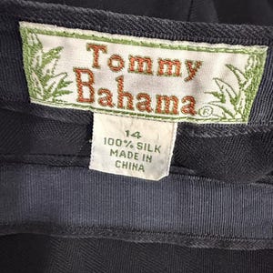 K&ouml;nnte beinhalten: Nahaufnahme eines marineblauen Kleidungsst&uuml;cketiketts mit dem Markennamen "Tommy Bahama" in orangefarbenen Buchstaben. Das Etikett gibt au&szlig;erdem an, dass das Kleidungsst&uuml;ck Gr&ouml;&szlig;e 14 hat und aus 100 % Seide besteht, hergestellt in China.