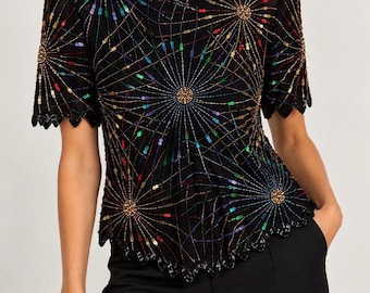 Può includere: Una camicetta nera a maniche corte con un vivace motivo multicolore ispirato ai fuochi d'artificio, realizzato con intricate perline e paillettes. Il capo presenta uno scollo rotondo e un orlo smerlato, abbinato a pantaloni neri.