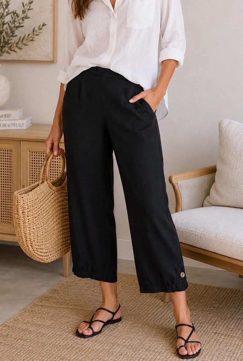 K&ouml;nnte beinhalten: Schwarze, cropped Hose mit Knopfdetail am Saum. Die Hose wird mit einem wei&szlig;en Hemd und schwarzen Sandalen kombiniert. Eine gewebte Tragetasche wird gehalten. Das Outfit ist l&auml;ssig und f&uuml;r warmes Wetter geeignet.