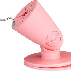 Puede incluir: Soporte para tel&eacute;fono rosa con base giratoria y bisagra. El soporte tiene una base circular y una parte superior c&oacute;nica con un hueco para un tel&eacute;fono. El soporte est&aacute; etiquetado como "Hinge".