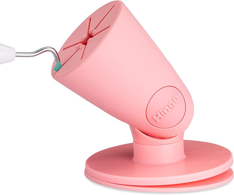 Puede incluir: Soporte para tel&eacute;fono rosa con base giratoria y bisagra. El soporte tiene una base circular y una parte superior c&oacute;nica con un hueco para un tel&eacute;fono. El soporte est&aacute; etiquetado como "Hinge".