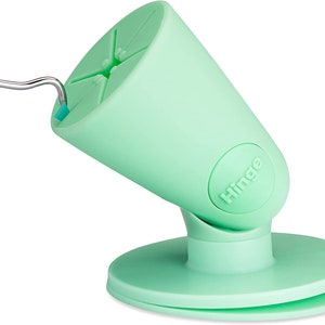 Puede incluir: Un soporte para tel&eacute;fono de color verde claro con una base de ventosa y un brazo articulado. El soporte tiene la palabra "Hinge" impresa en el lateral.