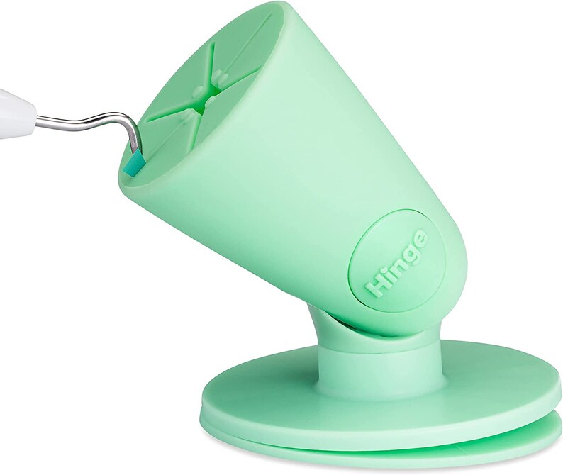 Puede incluir: Un soporte para tel&eacute;fono de color verde claro con una base de ventosa y un brazo articulado. El soporte tiene la palabra "Hinge" impresa en el lateral.