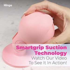 Może przedstawiać: R&oacute;żowa silikonowa przyssawka z okrągłą podstawą i kopułową g&oacute;rą. Tekst "Smartgrip Suction Technology" i "Watch Our Video To See It In Action!" jest nadrukowany r&oacute;żowym kolorem na białym tle.