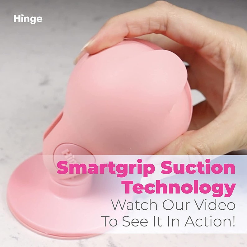 Może przedstawiać: R&oacute;żowa silikonowa przyssawka z okrągłą podstawą i kopułową g&oacute;rą. Tekst "Smartgrip Suction Technology" i "Watch Our Video To See It In Action!" jest nadrukowany r&oacute;żowym kolorem na białym tle.