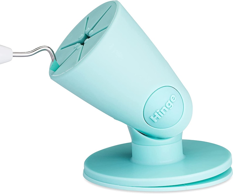 Puede incluir: Un soporte para tel&eacute;fono de color azul claro con un brazo articulado y una base de ventosa. El soporte tiene la palabra "Hinge" impresa en el lateral.