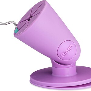 Puede incluir: Soporte para tel&eacute;fono morado con base de ventosa y bisagra. El soporte est&aacute; dise&ntilde;ado para sostener un tel&eacute;fono en posici&oacute;n vertical. El soporte tiene la palabra "Hinge" impresa en &eacute;l.