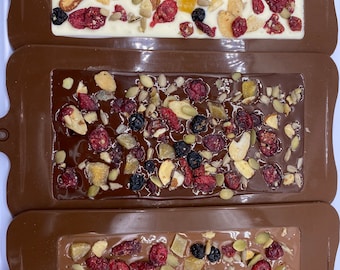 May include: Three silicone molds for making chocolate bark. The molds are brown and have a rectangular shape. Each mold is filled with white chocolate, dark chocolate, and milk chocolate bark. The bark is topped with dried cranberries, almonds, pumpkin seeds, and sunflower seeds.