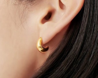 May include: Gold hoop earrings with a slightly curved shape. The earrings are worn in a person's ear.