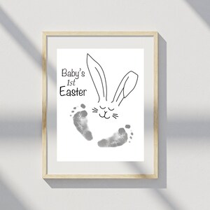 May include: A framed print featuring a black and white illustration of a bunny rabbit with the text "Baby's 1st Easter" and two grey baby footprints.