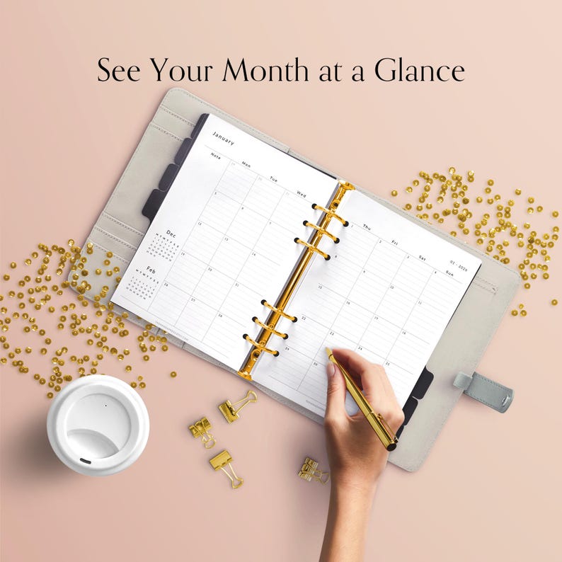 May include: A light grey planner open to a January calendar page, with a gold pen in hand, and the text "See Your Month at a Glance". The planner has gold accents. A white coffee cup and gold paper clips are also visible.