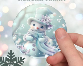 Könnte beinhalten: Ein Set aus sechs laminierten Weihnachtsaufklebern aus Vinyl. Die Aufkleber zeigen einen Schneemann mit Hut und Schal, mit floralen Akzenten. Der Text "Christmas Stickers" steht oben und "Set of 6 Vinyl Laminated Stickers" unten.