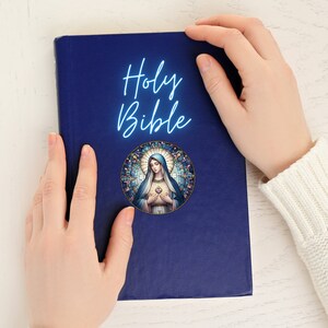 K&ouml;nnte beinhalten: Eine blaue, gebundene Heilige Bibel mit einem Buntglasbild der Jungfrau Maria auf dem Einband.