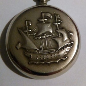 Pode incluir: Relógio de bolso de prata com uma gravação detalhada de um navio à vela na frente.