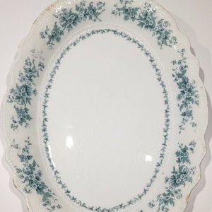 Könnte beinhalten: Eine weiße ovale Servierplatte mit einem gewellten Rand und einem grünen Blumendesign.