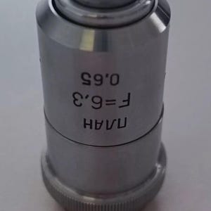 May include: A silver microscope objective lens with the text "UAAH F=9.3 0.65" printed on the side.